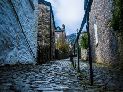 Cobblestone footpath with handrail in the centre. Old style houses line the footpath.